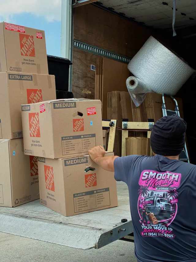 Mover with a stack of moving boxes beside the truck